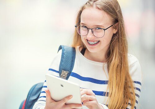 Portrait of a smiling beautiful teenage girl with dental braces. Young schoolgirl with school bag and tablet device.
